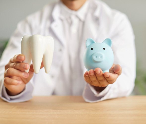 Dentist in white coat holding large model tooth and blue piggy bank