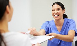Patient handing paperwork and pen to woman in blue scrubs