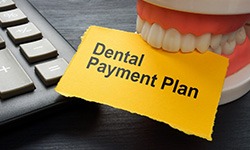 Artificial teeth next to calculator biting on paper that says “Dental Payment Plan”