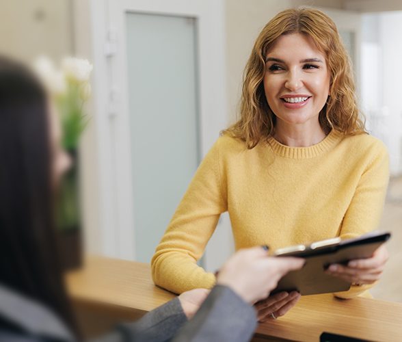Woman smiling and talking with the receptionist about dental insurance in Dallas